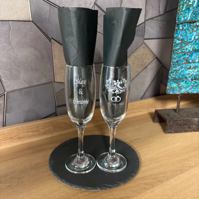 Gros plan d'un verre en cristal transparent gravé au laser avec motifs géométriques ou un monogramme détaillé, posé sur une surface de travail en atelier. Le verre personnalisé doit être clairement visible avec les détails de gravure distincts, illustrant la capacité d'L'GRAVE à personnaliser des pièces unitaires de haute qualité.