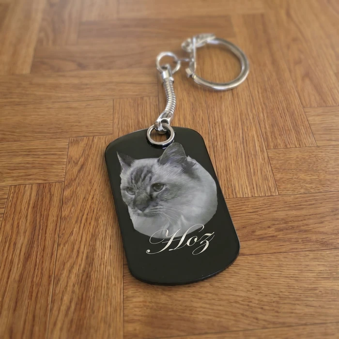 Porte-clés personnalisé en métal anodisé noir, format dog tag militaire, posé sur parquet en bois