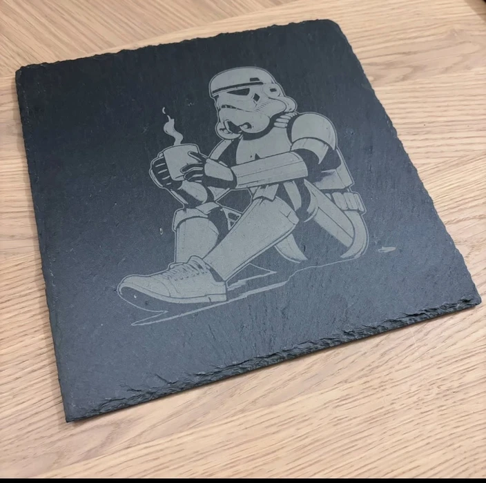 Plaque funéraire en granit noir poli, taillée en forme de cœur, posée sur socle transparent dans un jardin